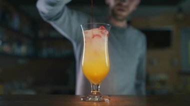 Barmen renkli karışıma yavaş çekimde sirop ekliyor.