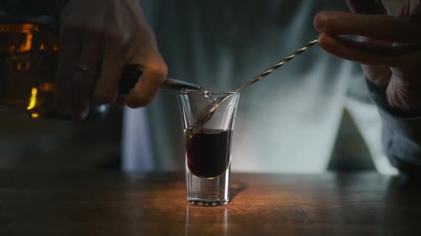 Barman schenkt transparante alcohol in de gelaagde shot met donkere drank — Stockvideo