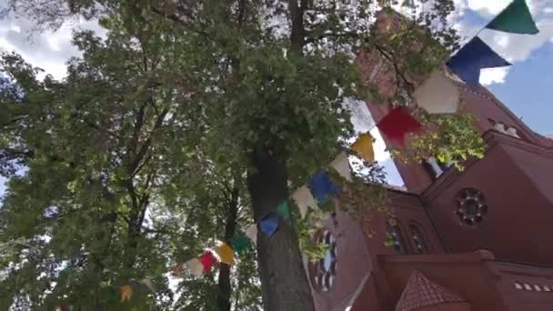 Vakantie decoraties fladderen in de wind bij de kerk op een zonnige dag — Stockvideo