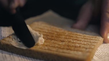 Aşçı, kızarmış ekmeğin üzerine bıçakla tereyağı sürer ve sandviç yapar.