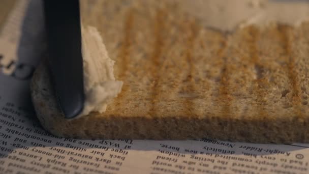 Повар размазывает ножом сливочное масло на хрустящем жареном хлебе, из которого получается сэндвич — стоковое видео