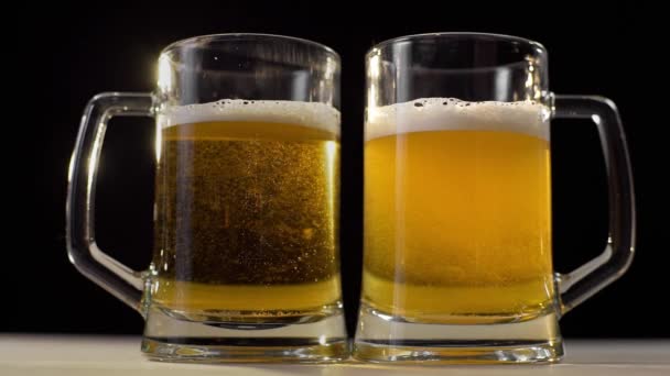 Zwei Biergläser mit goldenem Schaumbier auf schwarzem Hintergrund — Stockvideo