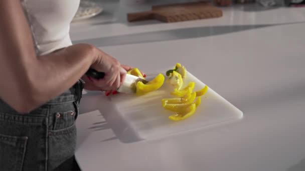 Mujer corta el pimiento amarillo con el cuchillo afilado en el tablero — Vídeos de Stock