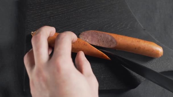 Kucharz kroi kiełbasę ostrym nożem na drewnianej desce — Wideo stockowe
