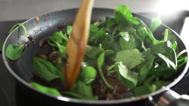 Повар готовит овощное блюдо с луком жареным в бальзамическом уксусе и добавляет шпинат — стоковое видео