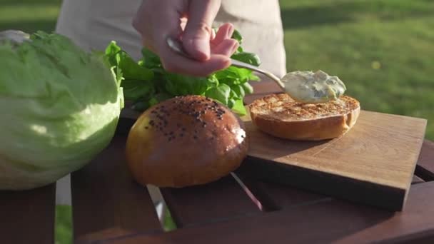 De kok doet saus op het broodje en maakt hamburger — Stockvideo