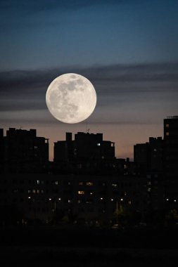 Şehir alacakaranlığı, binalar arasında dolunay var.