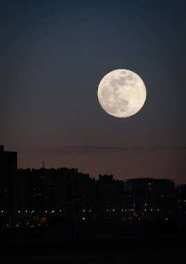 Şehir alacakaranlığı, binalar arasında dolunay var.