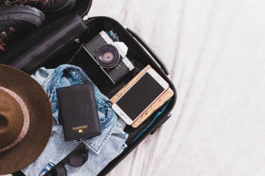 İçinde pasaport, fotoğraf makinesi, şapka, gözlük ve giysiler olan bavulu aç