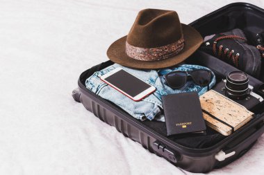 İçinde pasaport, fotoğraf makinesi, şapka, gözlük ve giysiler olan bavulu aç