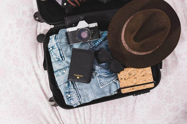 open suitcase with passport, photo camera, hat and glasses and clothes