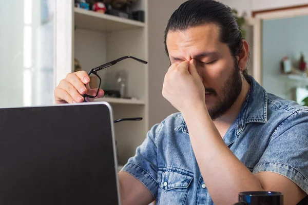 stressed young man rubs his eyes on telecommuting