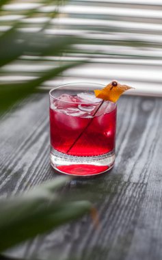 Pencerenin yanında kırmızı Negroni kokteyli ve klasik portakal kabuğu süslemesi.