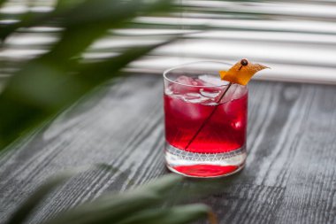 Pencerenin yanında kırmızı Negroni kokteyli ve klasik portakal kabuğu süslemesi.