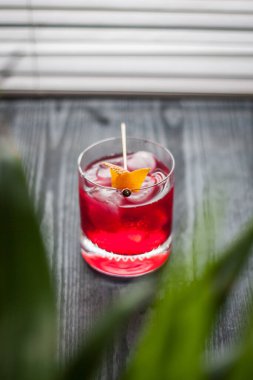 Pencerenin yanında kırmızı Negroni kokteyli ve klasik portakal kabuğu süslemesi.