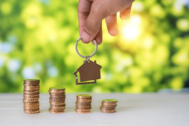 Adamın el ele tutuşması ev şeklindeki anahtarlığı yeşil bokeh arka planlı altın paraların üzerinde. Emlak yatırım kavramı.