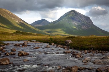 Sligachan nehri ön planda, Marsco zirvesine çıkıyor. Kızıl Tepeler 'de (Red Cuillin) İskoçya yazının kasvetli öğleden sonrası sahnesi. Yamaçlarda güzel ışık oyunları var Bulutlar ve alçak güneş sayesinde.