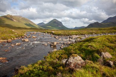 Sligachan nehri ön planda, Marsco zirvesine çıkıyor. Kızıl Tepeler 'de (Red Cuillin) İskoçya yazının kasvetli öğleden sonrası sahnesi. Yamaçlarda güzel ışık oyunları var Bulutlar ve alçak güneş sayesinde.