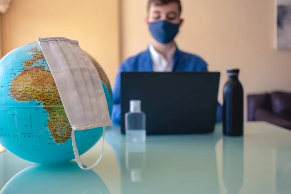 Earth with a face mask and Business man on a desk working with a mask on the background working on a computer.