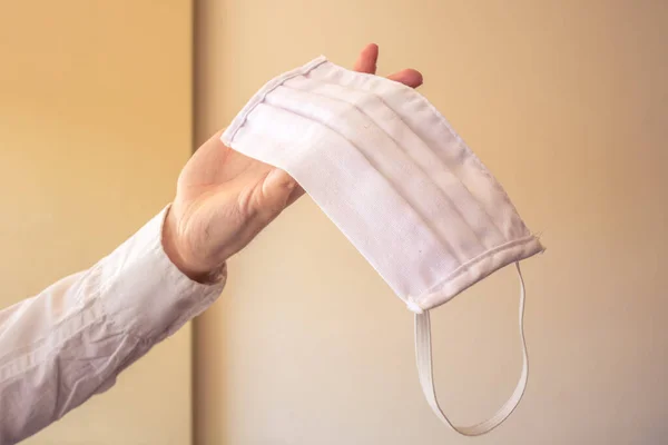 El ele tutuşarak, kumaştan yapılmış beyaz bir maske. Yani maskenin önleme, salgın hastalıklar ya da tıbbi durumlar için kullanımı..