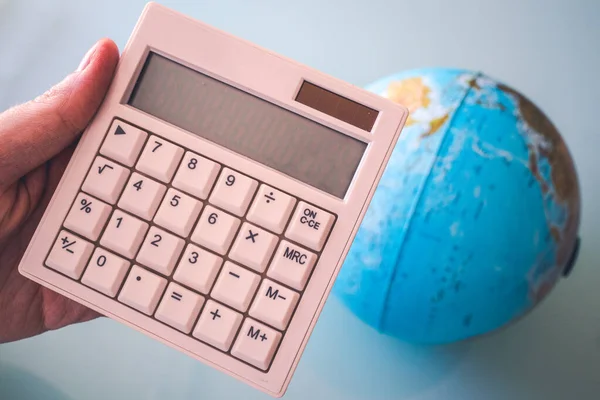 Ekranda herhangi bir sayı olmayan beyaz bir hesap makinesini tutan el oraya bir şey koymak için mükemmel. Ve arka planda bir dünya topu.