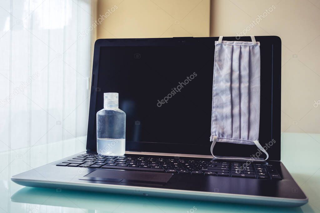 Photo of a laptop with cleaning and health objects such as face mask or disinfectant. Symbolizing new way of working at home.