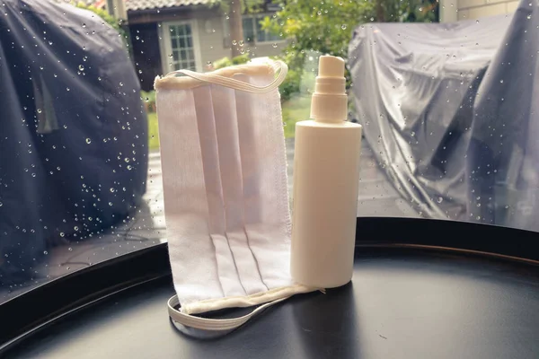 Evde yağmurlu bir günde pencerenin yanında yüz maskesi ve dezenfektan..