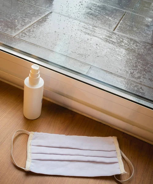 Evde yağmurlu bir günde pencerenin yanında yüz maskesi ve dezenfektan..