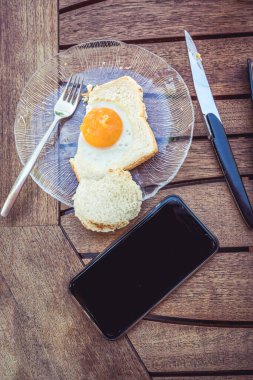 İş kahvaltısı. Ahşap bir masada telefonlu bir yumurta.