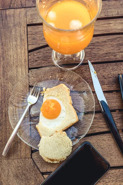 Tabakta yumurtalı sandviç, çatal ve bıçak. Bir bardak portakal suyu.