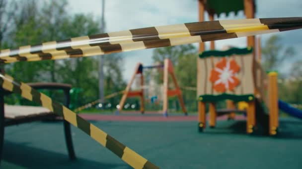 Lonely taped children playground. An empty swing sways in the wind in a pandemic — Stock Video