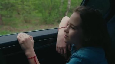 Arabayla seyahat eden bir kız, temiz hava almak için pencereyi açıyor.