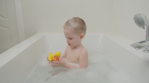 Cheerful boy playing bathroom with foam and toys. Baby with blue eyes and blond — Stock Video