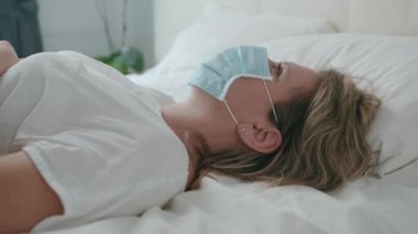 Yatakta yatan maskeli kadın üzgün ve kederli hasta gözler, virüs...