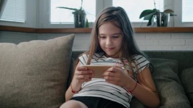Kesilmiş güzel bir kız. Kanepede oturan akıllı bir telefonla oynuyor.