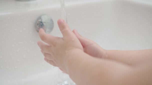 Маленький ребенок моет руки с мылом над раковиной с водой COVID-19. Крупный план — стоковое видео