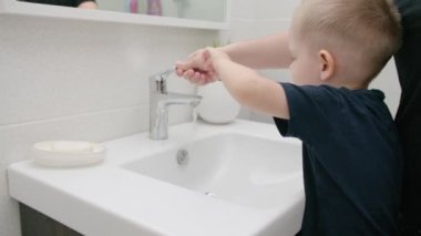 Anne, küçük çocuğun musluğu yıkaması için suyla açmasına yardım et. Sağlık kavramı