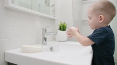 Küçük çocuk ellerini lavabonun üzerinde sabunla yıkıyor. COVID-19 'a karşı koruma