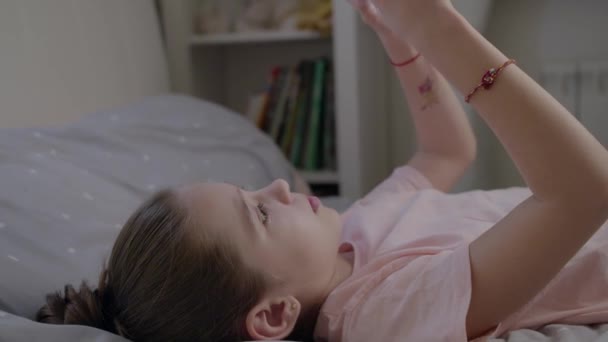 Bambina carina gioca in smartphone sdraiato sul letto — Video Stock