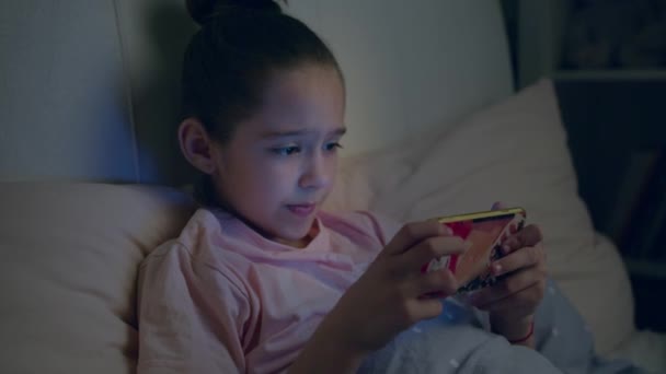 침대에 누워 스마트폰으로 귀여운 여자 아이가 놀고 있습니다 — 비디오