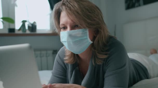 Femme couchée sur le lit travaillant avec un ordinateur portable dans le coronavirus masque — Video