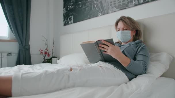 Γυναίκα ξαπλωμένη στο κρεβάτι άρρωστη και διαβάζει ένα βιβλίο και φτερνίζεται από τον κορωναϊό. — Αρχείο Βίντεο