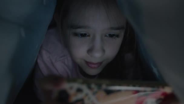 Küçük kız duygusal olarak gece battaniyenin altında akıllı telefonda oynuyor. — Stok video