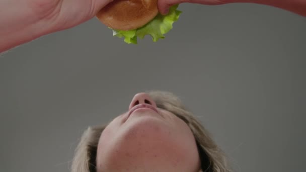 Een meisje in een roze T-shirt bijt in een hamburger. Het uitzicht van onderen. Langzaam in beweging — Stockvideo