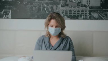 Dizüstü bilgisayarlı, maskeli bir kız internette Coronavirus hakkında konuşuyor.