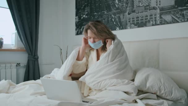Жінка сидить на ліжку під ковдрою, працює над маскою коронавірус — стокове відео