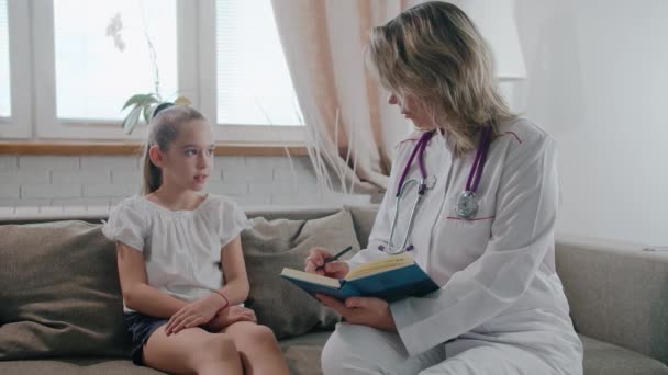 Pediatra pediatra completa uma linda garota bonita sobre sua condição de saúde e escreve sintomas. Conceito de saúde infantil — Vídeo de Stock
