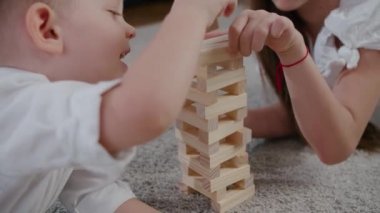 Beyaz kız ve oğlan güneşli bir günde evde jenga oynuyorlar, birlikte gülüyorlar ve eğleniyorlar. Yakın çekim ve yavaş çekim kamerası.