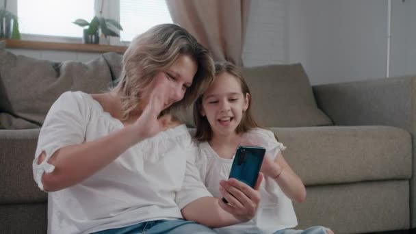 Glad kaukasiska familj mamma och söt liten unge dotter skratta använda smartphone på distans prata roligt ansikte och le slow motion — Stockvideo