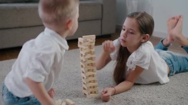 Beyaz kız ve oğlan güneşli bir günde evde Jenga oynuyorlar, birlikte gülüyorlar ve eğleniyorlar.